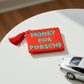 Monedero de cuentas rojo con el mensaje MONEY FOR PORSCHE en cuentas azules encima de una mesa con un coche de juguete al lado