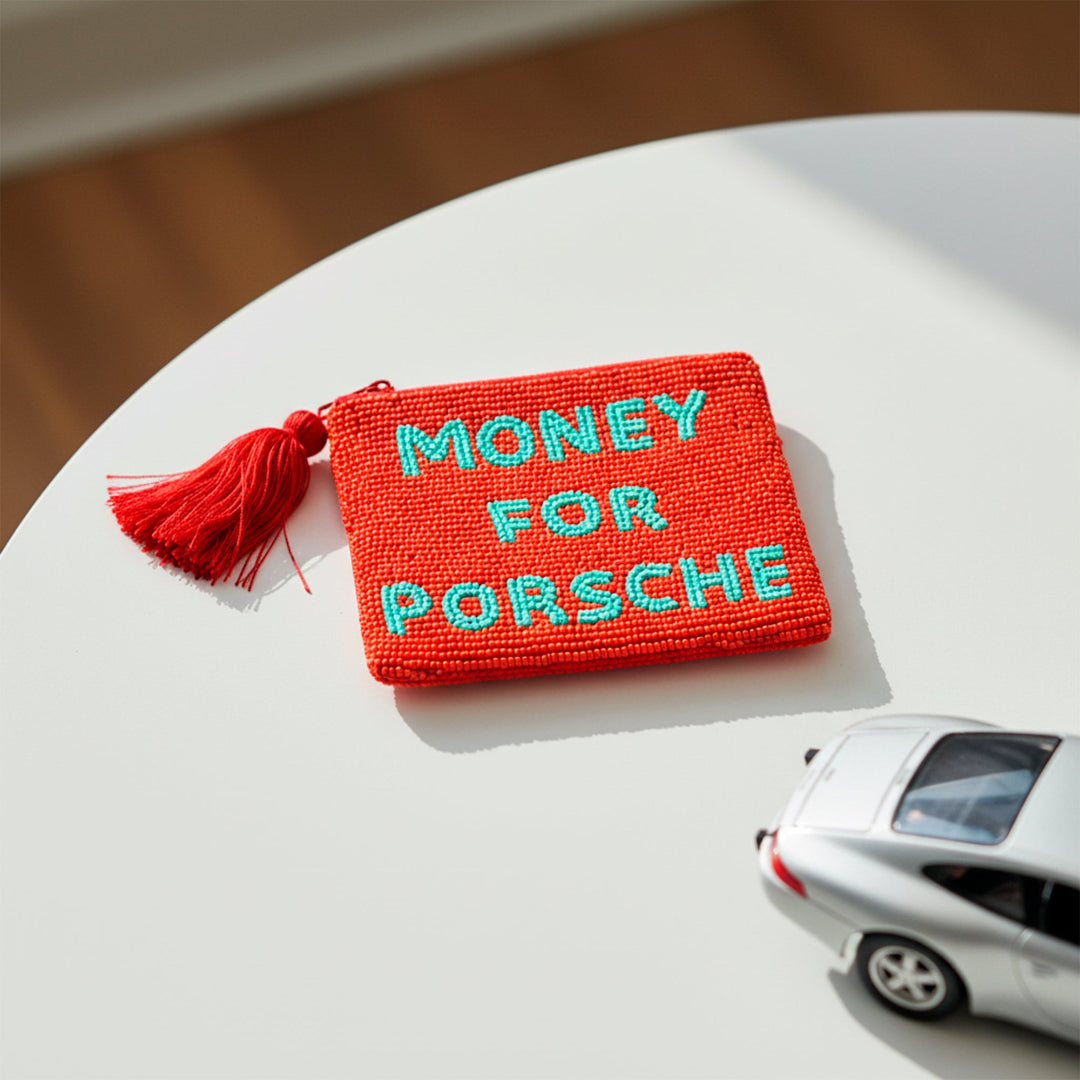 Monedero de cuentas rojo con el mensaje MONEY FOR PORSCHE en cuentas azules encima de una mesa con un coche de juguete al lado