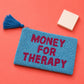 Monedero de cuentas azules y rosas con el mensaje MONEY FOR THERAPY sobre  una mesa rosa con un taco de post its al lado