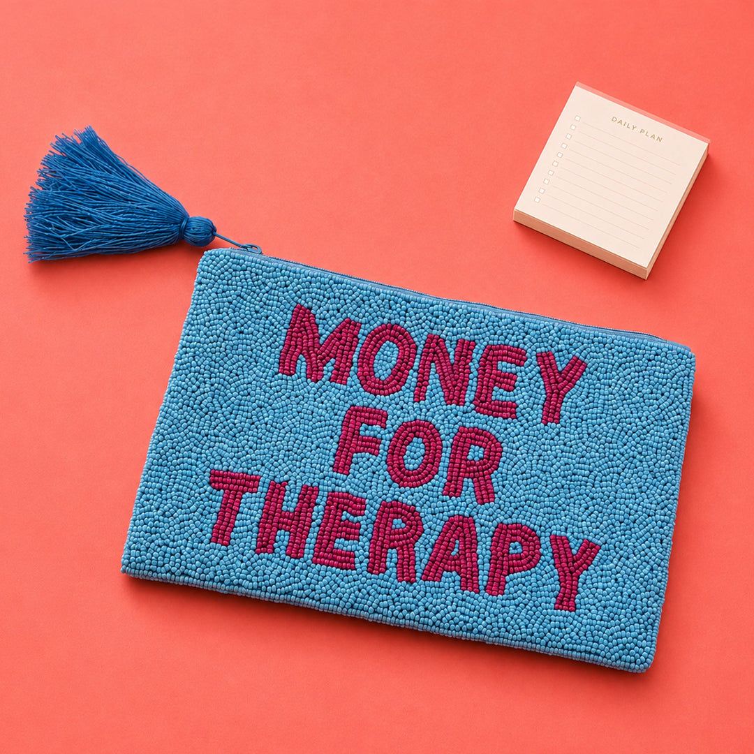 Monedero de cuentas azules y rosas con el mensaje MONEY FOR THERAPY sobre  una mesa rosa con un taco de post its al lado