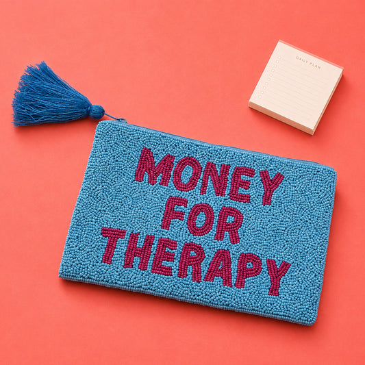 Monedero de cuentas azules y rosas con el mensaje MONEY FOR THERAPY sobre  una mesa rosa con un taco de post its al lado