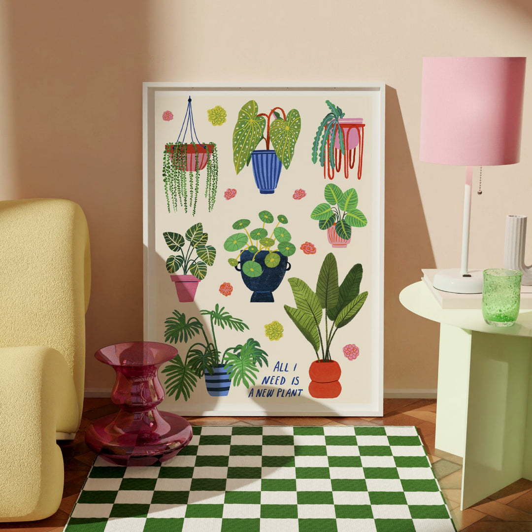 Ilustración grande enmarcada en blanco de varias plantas y el mensaje "All I need is a new plant" con letra manuscrita puesta sobre el suelo en una casa con muebles de diseño
