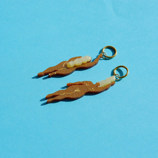 pendientes de metacrilato con aro dorado de la artista mitumi con dos mujeres nadando desnudas en color marrón con el pelo rubio y sobre fondo azul