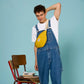 Hombre con mono vaquero y sillas de colegio con la Riñonera de algodón orgánico en color amarillo de la marca francesa Hindbag