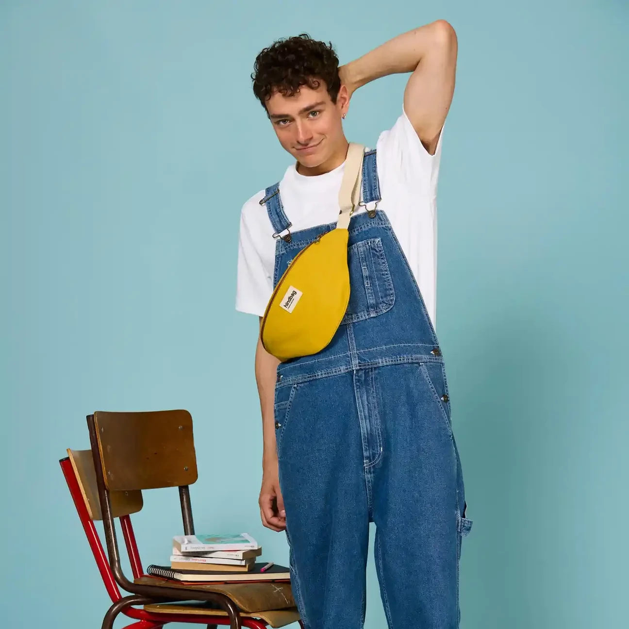Hombre con mono vaquero y sillas de colegio con la Riñonera de algodón orgánico en color amarillo de la marca francesa Hindbag