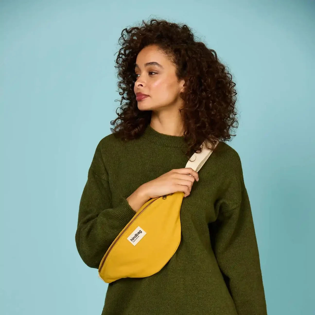Mujer con vestido de punto verde y riñonera de algodón orgánico en color amarillo de la marca francesa Hindbag