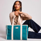 Mujer sentada en el suelo con el bolso grande y cuadrado estilo tote bag de color azul turquesa con asas beige para llevar al hombro de la marca Hindbag