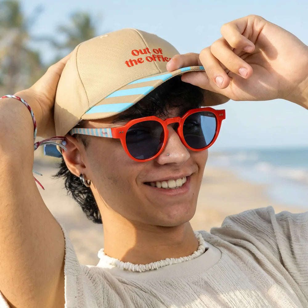 modelo posando con las gafas de sol de Fisura del modelo Out of the office redondas con la parte delantera roja y las patillas a rayas azules y marrones