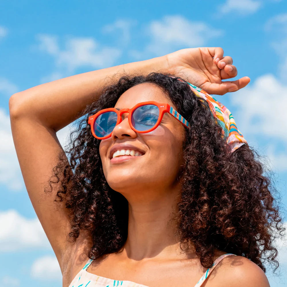 modelo posando con las gafas de sol de Fisura del modelo Out of the office redondas con la parte delantera roja y las patillas a rayas azules y marrones