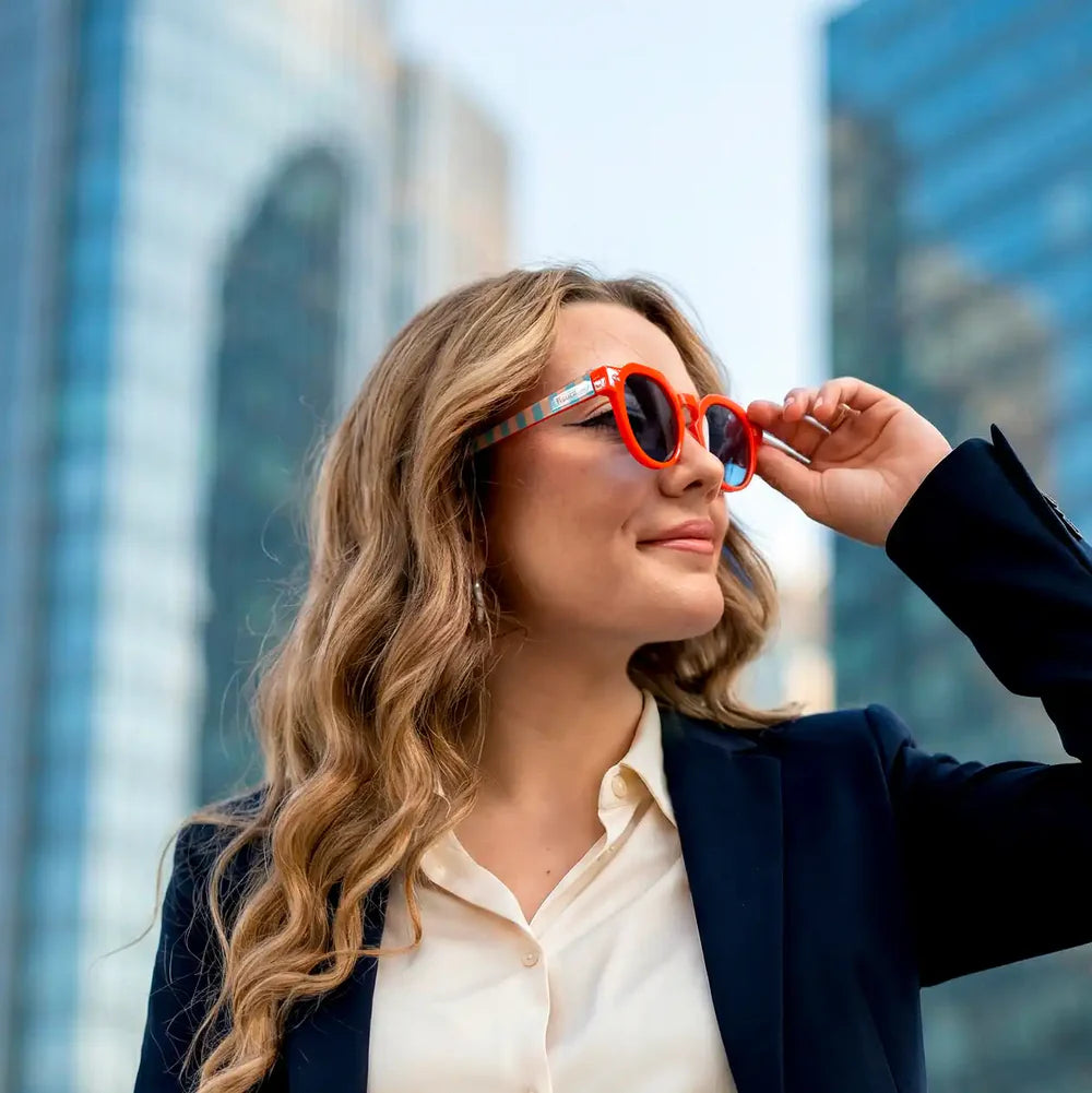 modelo posando con las gafas de sol de Fisura del modelo Out of the office redondas con la parte delantera roja y las patillas a rayas azules y marrones