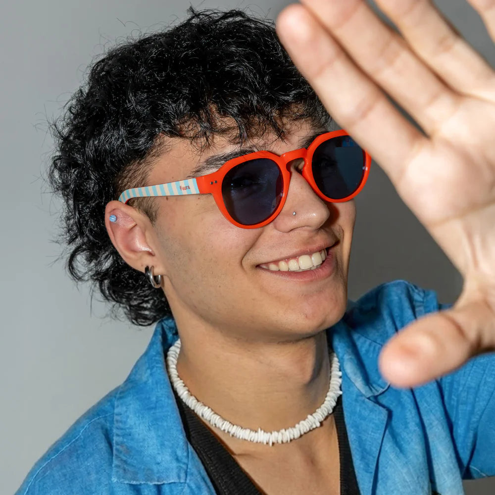 modelo posando con las gafas de sol de Fisura del modelo Out of the office redondas con la parte delantera roja y las patillas a rayas azules y marrones