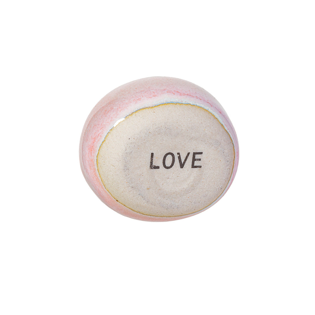 Parte trasera de la piedrecita rosa con el texto "LOVE" escrito, sobre fondo blanco. 