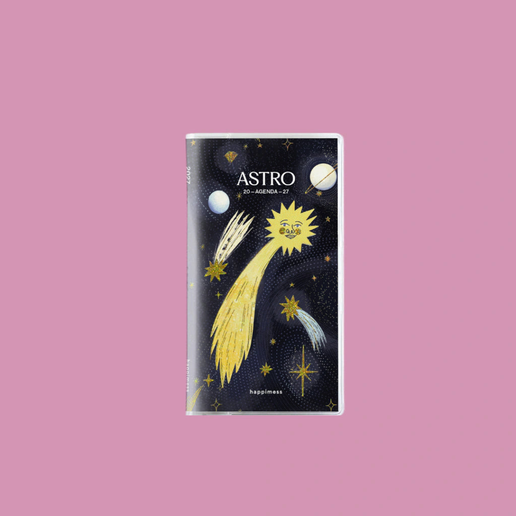 Agenda pocket Astro 2027 de Happimess con portada negra, estrella fugaz dorada y sol con cara, fondo rosa claro
