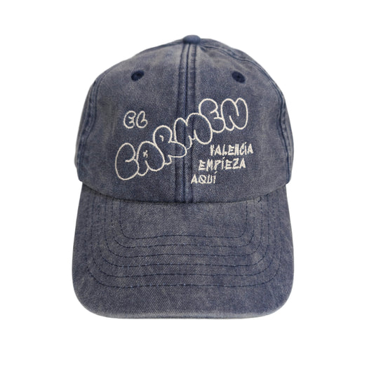 parte frontal de una gorra azul con el texto "El Carmen, Valencia empieza aquí" bordado en color blanco