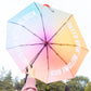 Paraguas plegable con esqueleto negro y estampado degradado de colores con el mensaje Hello rain, welcome back en letras mayúsculas blancas visto desde el interior