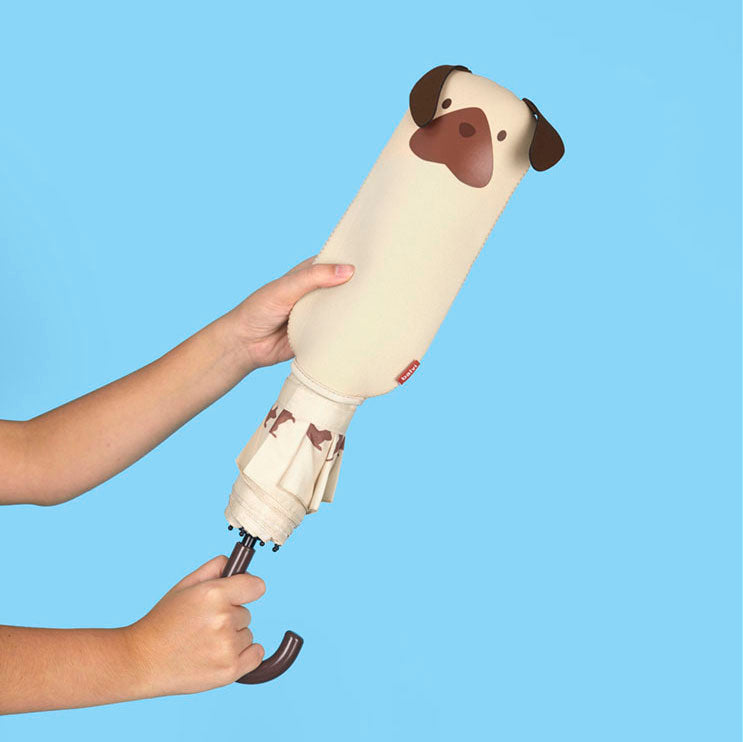 Paraguas plegable con funda de neopreno en forma de cachorro beige con orejas marrones, sostenido por dos manos sobre fondo azul