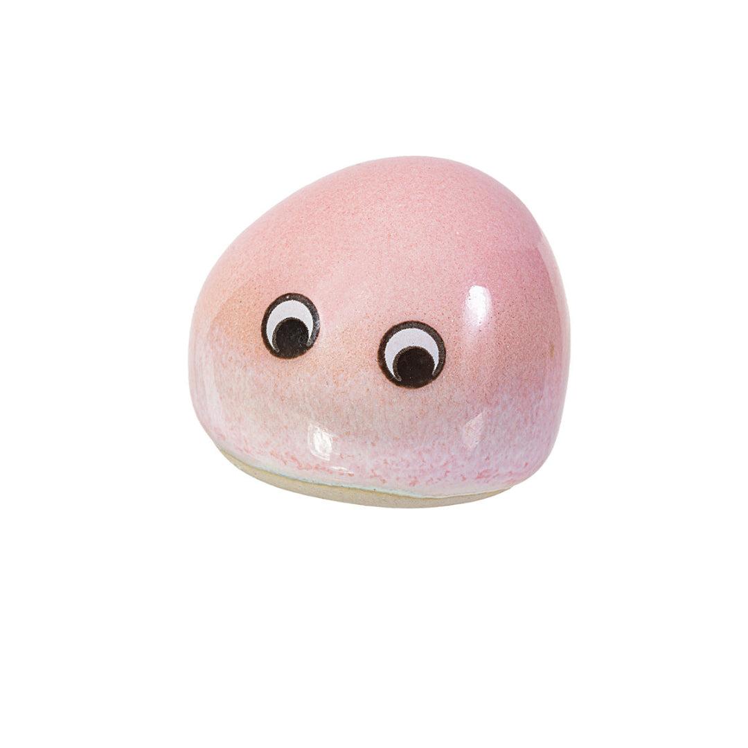 Piedrecita rosa con ojos sobre fondo blanco.