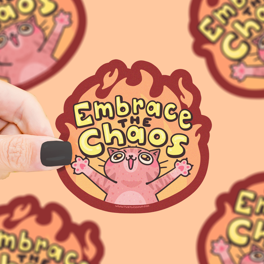 Pegatina de gato con las patas delanteras abiertas, y fuego detrás con la frase "Embrace the chaos" arriba.