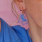 Primer plano de la oreja de una mujer con camiseta azul y pendientes de aro con forma de tumbona de playa a rayas azules