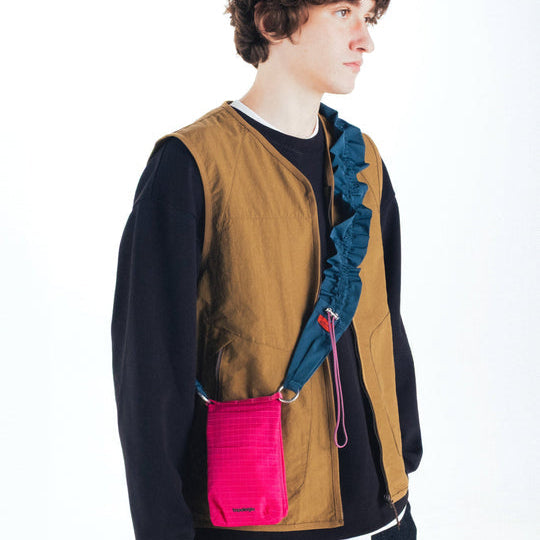 Chico con el bolso pequeño para llevar el móvil de Topologie en color rosa fucsia con tejido ripstop colgado en bandolera