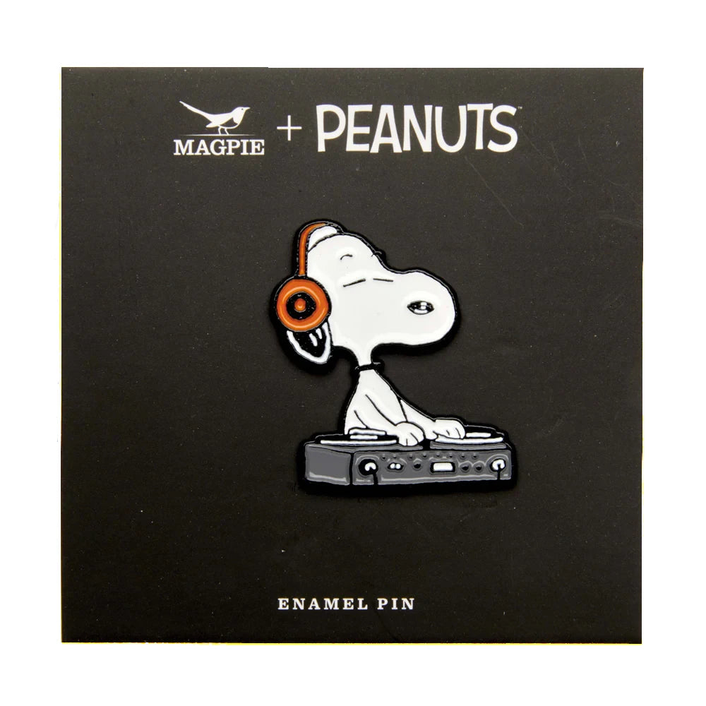 Pin de metal con forma de perro Snoopy con cascos de DJ pinchando en una mesa de mezclas sobre cartón negro con el logo de Peanuts y Magpie