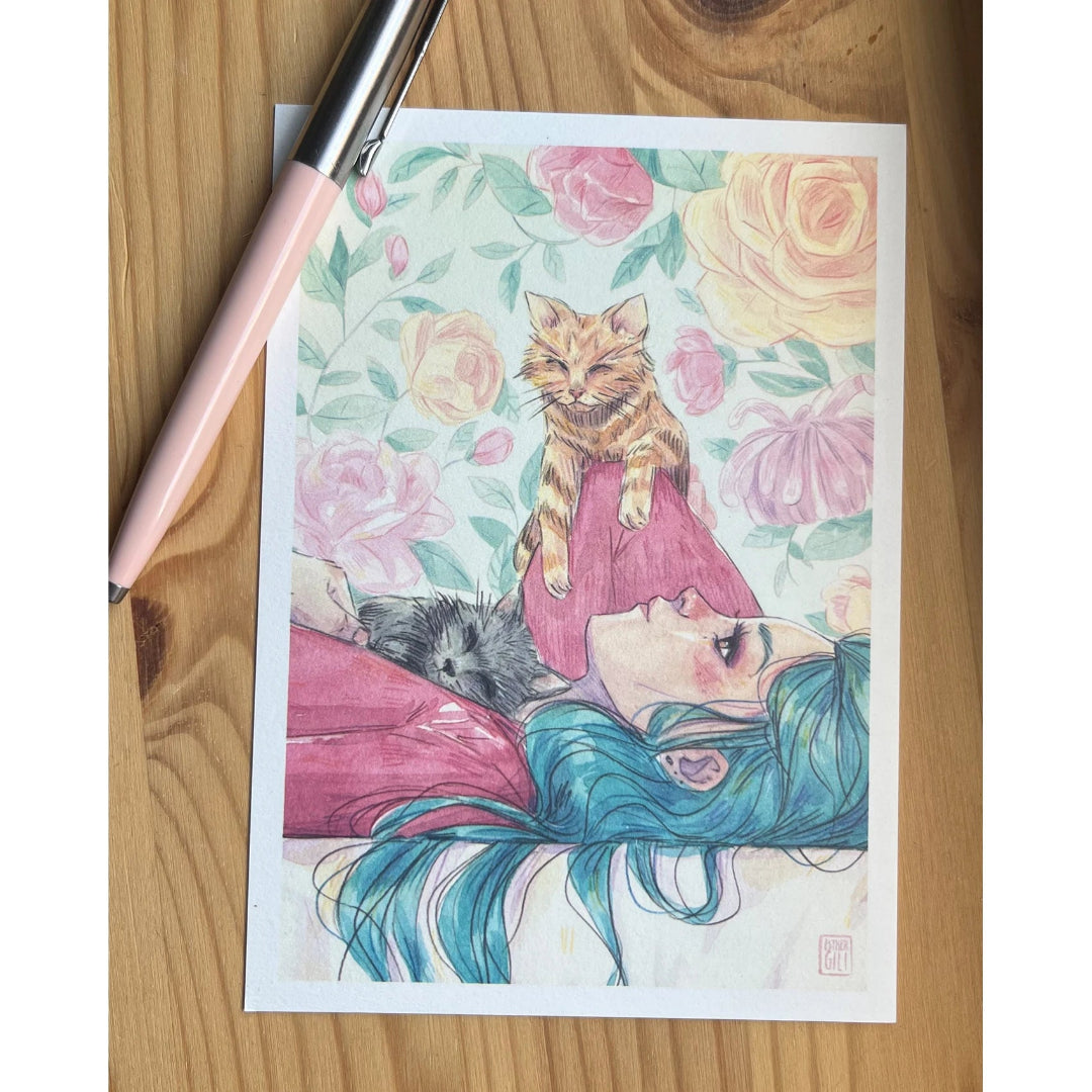 Postal con ilustración de Esther Gili de una chica tumbada con dos gatos encima y una pared con papel pintado de rosas de fondo