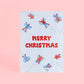Tarjeta de Navidad plantable de Resetea, con ilustración de ocho personas haciendo ángeles de nieve tumbados en el suelo y el mensaje MERRY CHRISTMAS centrado en rojo