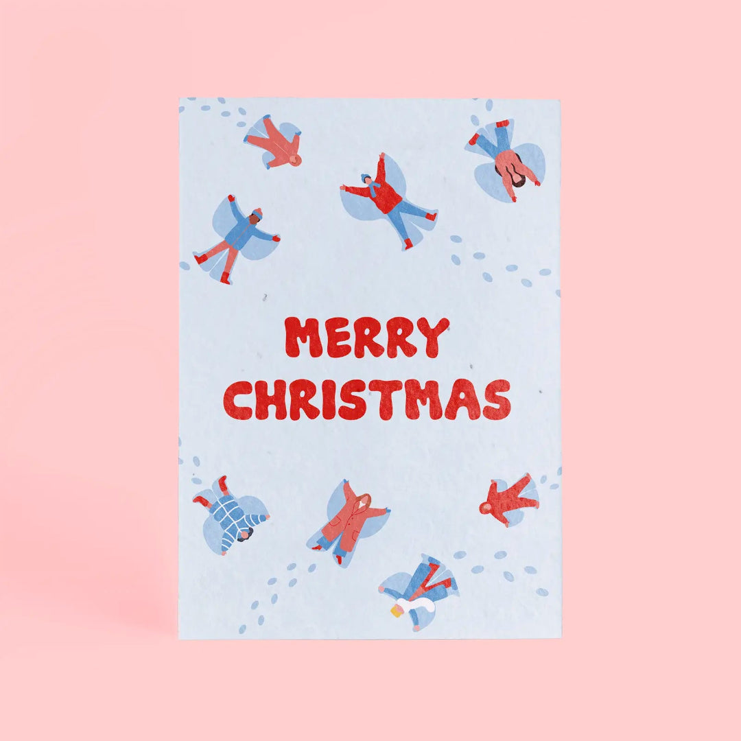 Tarjeta de Navidad plantable de Resetea, con ilustración de ocho personas haciendo ángeles de nieve tumbados en el suelo y el mensaje MERRY CHRISTMAS centrado en rojo