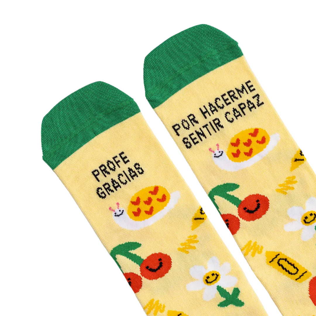 Detalle de la puntera de los calcetines estampados con dibujos de flores, manzanas, lápices, cerezas y caracoles con el mensaje Profe gracias por hacerme sentir capaz