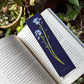 Libro abierto sobre plantas con un marcapáginas azul oscuro con ilustración de flores de nomeolvides morados