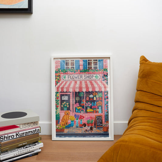 Salón de una casa con un puzzle enmarcado de 1000 piezas con ilustración de la fachada de una floristería y dos perritos
