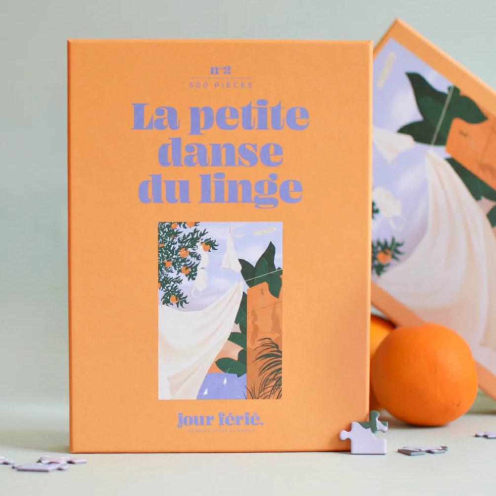 Caja de puzzle de 500 piezas de color naranja donde vemos una rama de un naranjo y una sábana blanca tendida. 