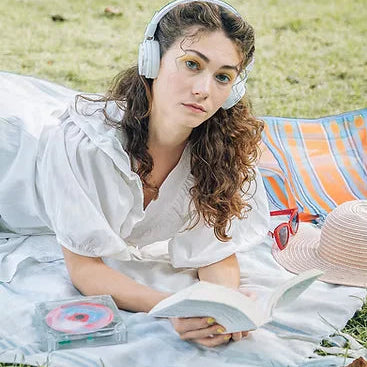 Chica leyendo en el parque y escuchando música con altavoces bletooth y el Reproductor de CD transparente de Ninm Lab