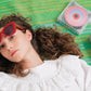Chica tmbada en una manta verde con gafas de sol y el reproductor de CD transparente de Ninm Lab sonando al lado