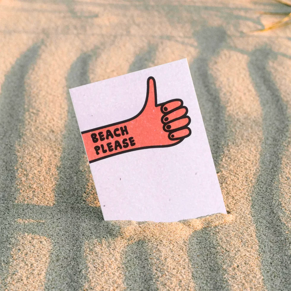 postal con semillas dentro de la marca resetea con un puño cerrado levantando el pulgar con el texto Beach please, en la playa