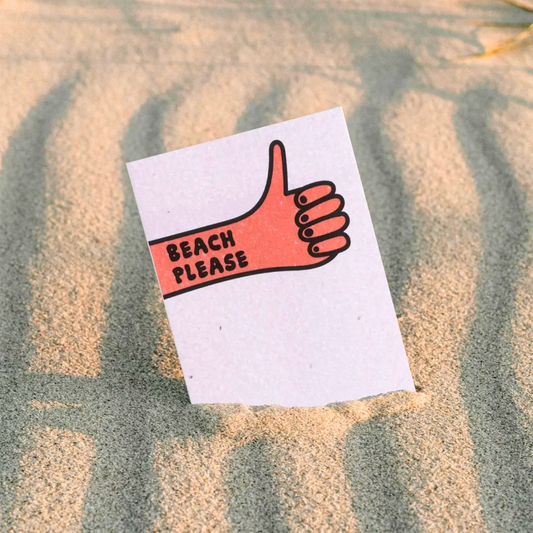 postal con semillas dentro de la marca resetea con un puño cerrado levantando el pulgar con el texto Beach please, en la playa