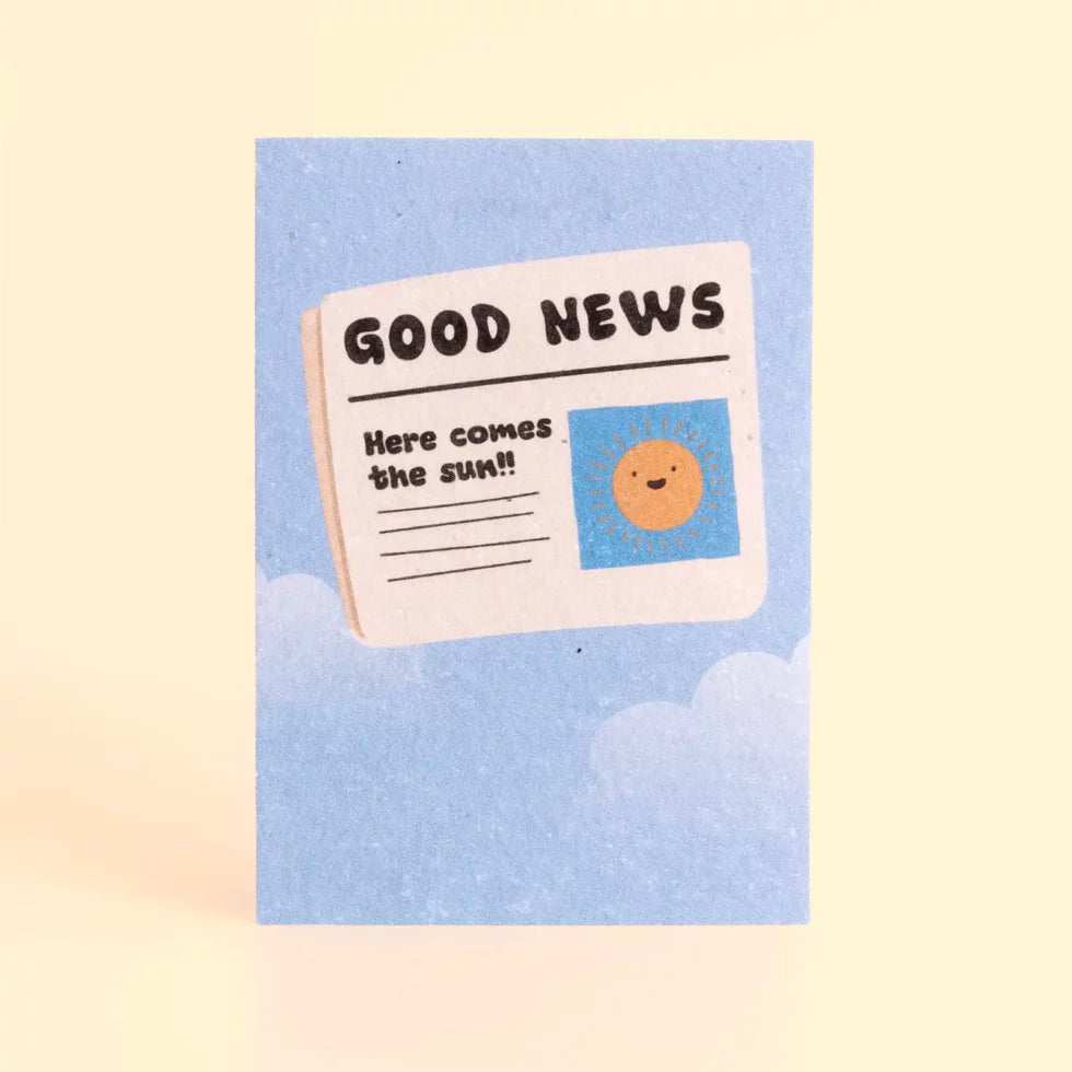 postal con semillas dentro de la marca resetea con el fondo azul y un dibujo de un periódico con un sol sonriente y el texto Good news, here comes the sun!! 