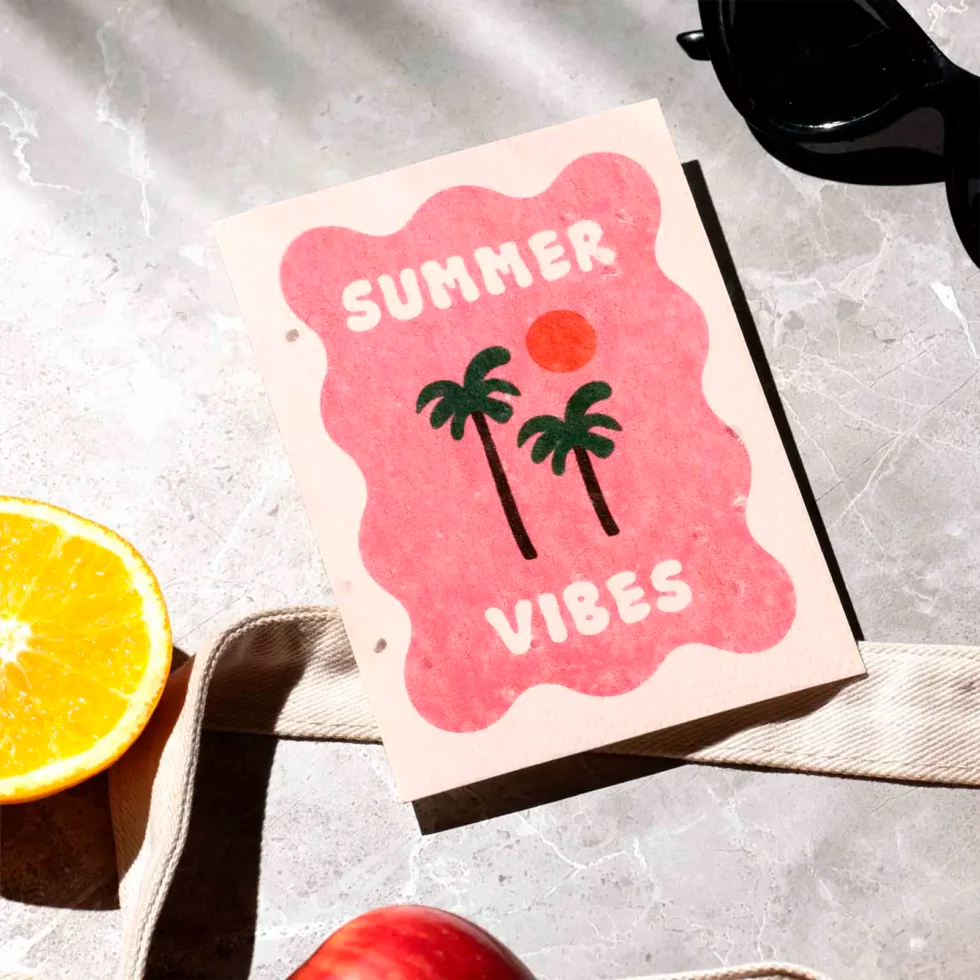 postal con semillas dentro de la marca resetea con un cuadraro en color rosa con dos palmeras y un sol y el texto Summer Vibes en blanco. Con unas gafas de sol y fruta alrededor