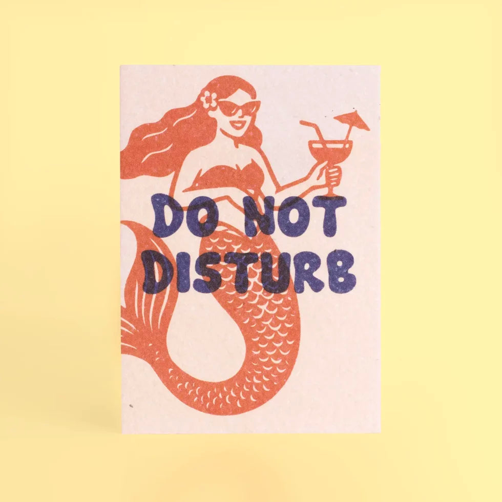 postal con semillas dentro de la marca resetea con una sirena sonriendo con gafas de sol y una bebida en la mano dibujada en color rojo con el texto Do Not Disturb en color azul