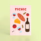 postal con semillas dentro de la marca resetea con dibujos de una barra de pan, dos gildas tomate, queso, copas de vino y una botella de vino y el texto PICNIC