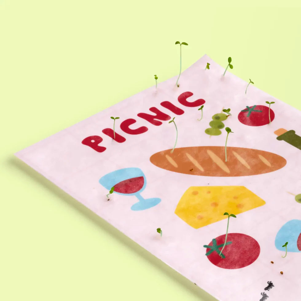detalle de la postal con semillas dentro de la marca resetea con dibujos de una barra de pan, dos gildas tomate, queso, copas de vino y una botella de vino y el texto PICNIC con brotes saliendo de ella