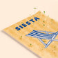 detalle de la postal con semillas dentro de la marca resetea con el fondo a rayas amarillas, una tumbona a rayas dibujada en azul y el texto SIESTA también en azul con brotes saliendo de ella