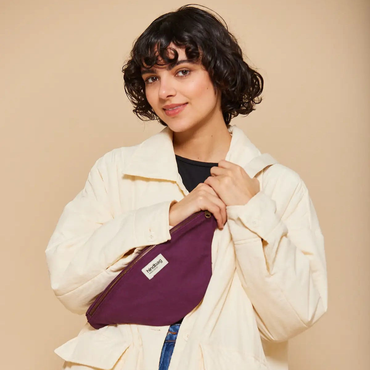 Mujer con abrigo beige y la riñonera color ciruela de la marca francesa Hindbag