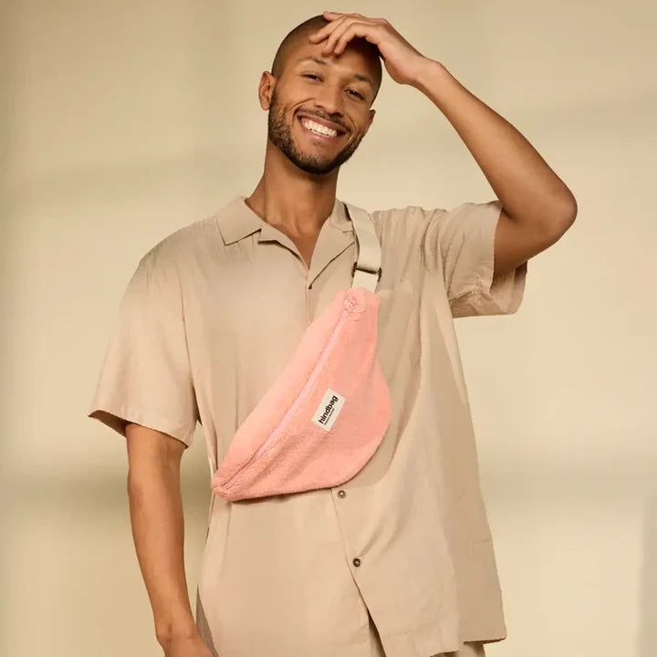 Hombre vestido de beige con una riñonera de rizo rosa de la marca francesa Hindbag