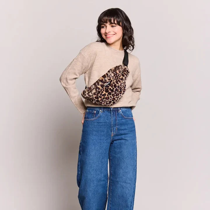 Mujer con vaqueros y jersey con la riñonera con tejido de peluche y estampado animal print de leopardo de la marca francesa Hindbag