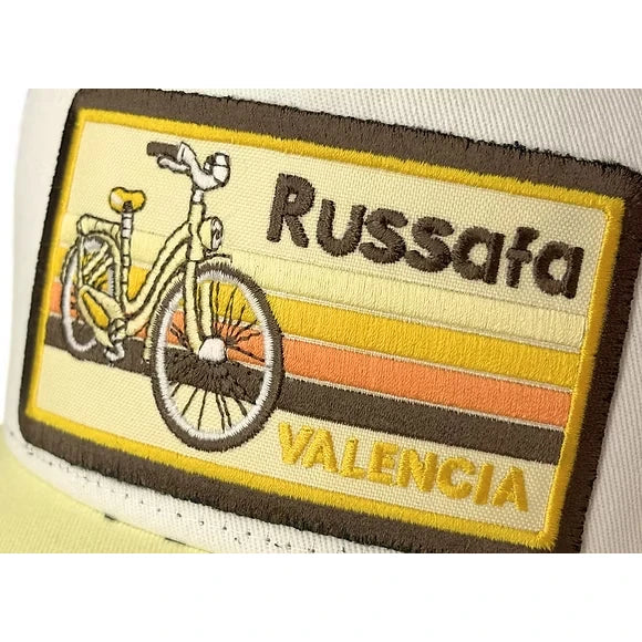 Primer plano de la gorra blanca y crema  con rejilla negra y parche bordado del barrio de ruzafa con una bicicleta