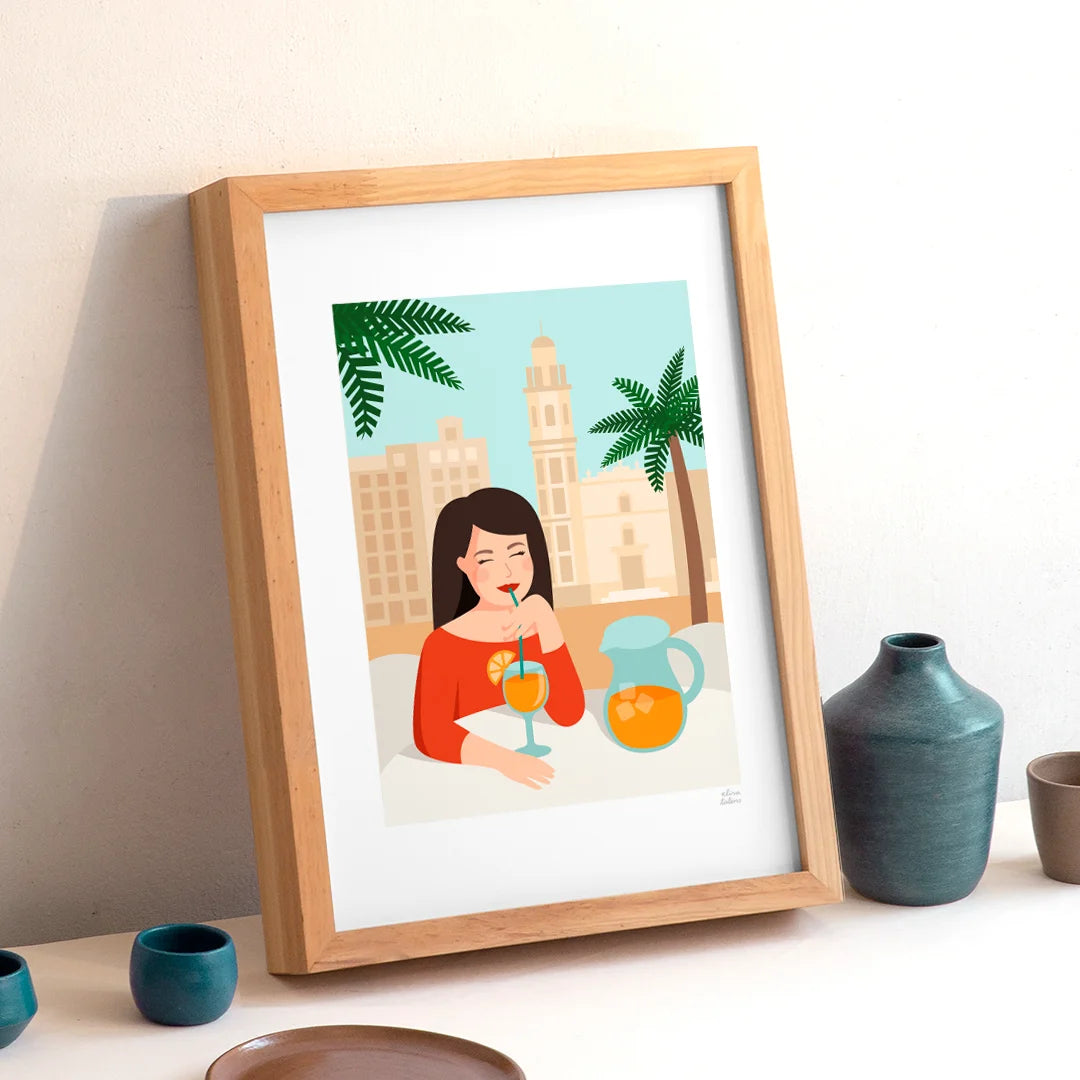 Lámina enmarcada de la ilustradora Elisa Talens mostrando una chica tomando un refresco sentada en una mesa y con una palmera y el campanario de San Valero en Ruzafa (Valencia) por detrás