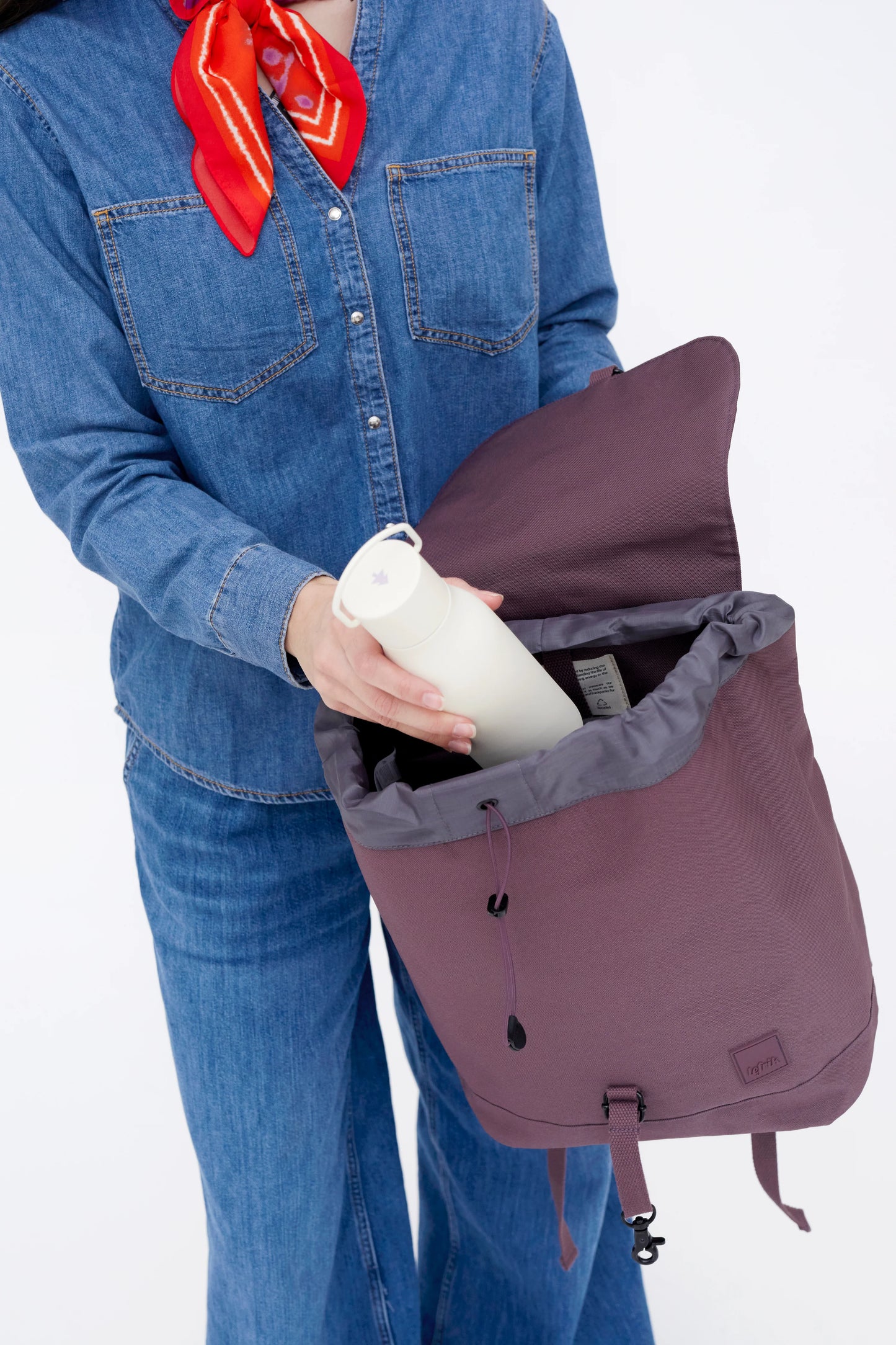 Mujer metiendo una botella de agua en una mochila Scout espaciosa, impermeable y reciclada color morado berenjena de la marca española Lefrik