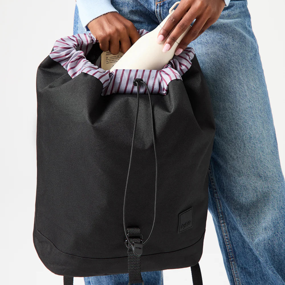 Chica con pantalones vaqueros metiendo una botella de agua en la mochila negra reciclada de Lefrik