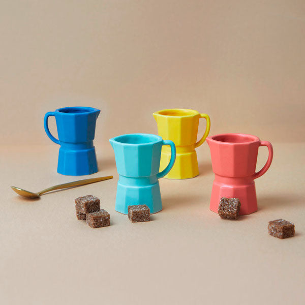 Juego de cuatro tazas de café expreso solo de cerámica de diferentes colores: azul, rosa, amarillo y turquesa junto a terrones de azúcar moreno y una cucharilla de café